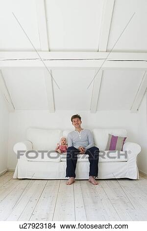 Picture - Portrait of mature father sitting next to baby daughter on sofa. Fotosearch