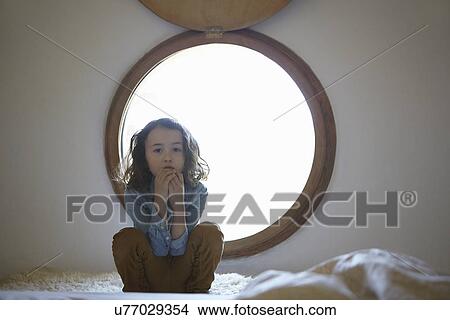Portrait of sullen girl crouching in front of circular window View Large Photo Image Picture - Portrait of sullen girl crouching in front of circular window. Fotosearch