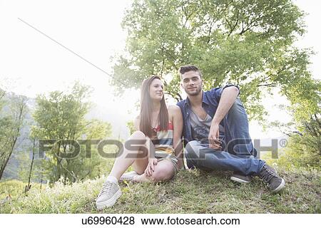 Stock Photo - Portrait of young couple sitting on grass, Piemonte, Italy. Fotosearch