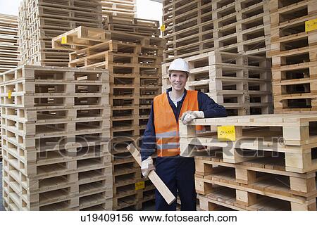 Stock Photograph - Portrait of young male worker and pallet stacks in timber yard. Fotosearch
