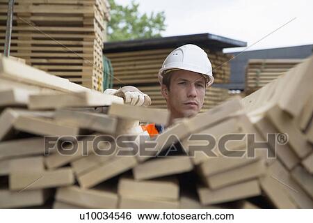 Stock Photograph - Portrait of young male worker behind wood planks in timber yard. Fotosearch
