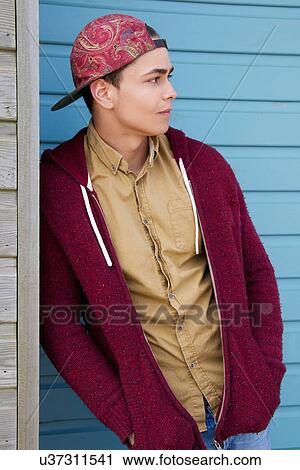 Stock Image - Portrait of young man leaning against beach hut. Fotosearch