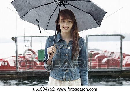 Stock Image - Portrait of young woman by lake with umbrella. Fotosearch