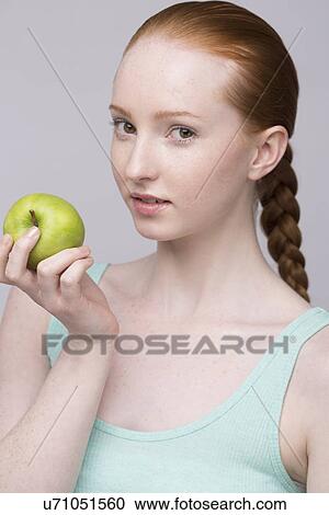 Stock Image - Portrait of young woman, holding green apple. Fotosearch