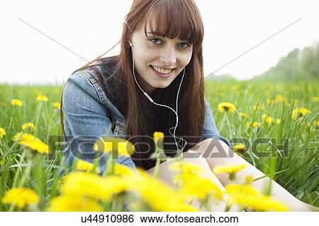 Stock Photograph - Portrait of young woman in earphones in dandelion field. Fotosearch