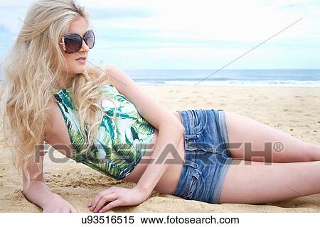 Stock Photography - Portrait of young woman in sunglasses lying on beach. Fotosearch