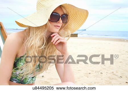 Stock Photography - Portrait of young woman in sunhat and sunglasses at beach. Fotosearch