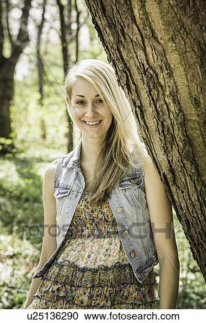 Portrait of young woman leaning against tree in forest View Large Photo Image Stock Image - Portrait of young woman leaning against tree in forest. Fotosearch