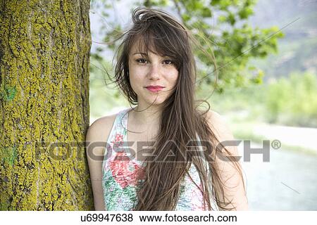 Portrait of young woman leaning against tree trunk View Large Photo Image Stock Photo - Portrait of young woman leaning against tree trunk. Fotosearch