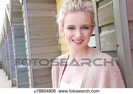Stock Photograph - Portrait of young woman leaning against beach hut. Fotosearch