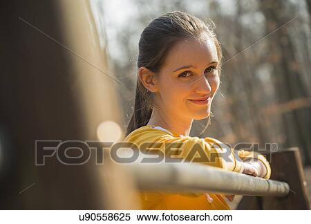 Stock Photography - Portrait of young woman leaning on fence in forest. Fotosearch