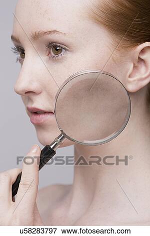 Stock Photo - Portrait of young woman, magnifying glass on cheek. Fotosearch