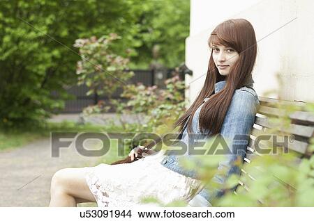 Portrait of young woman sitting on garden bench View Large Photo Image Picture - Portrait of young woman sitting on garden bench. Fotosearch