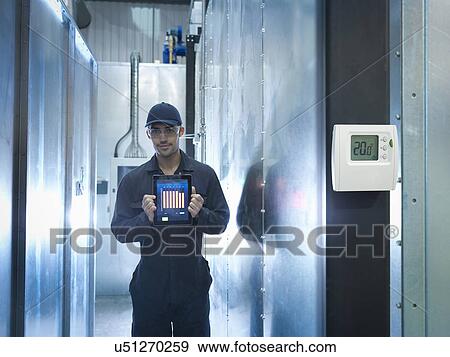 Stock Photo - Proud factory worker showing energy saving on digital tablet in factory, portrait. Fotosearch