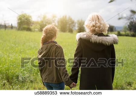 Stock Image - Rear view of mother and teenage daughter holding hands. Fotosearch