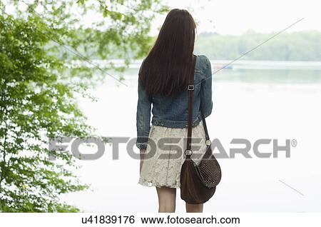 Rear view of young woman next to lake View Large Photo Image Stock Photograph - Rear view of young woman next to lake. Fotosearch