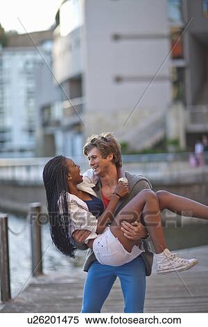 Stock Photography - Romantic young man carrying girlfriend in arms. Fotosearch
