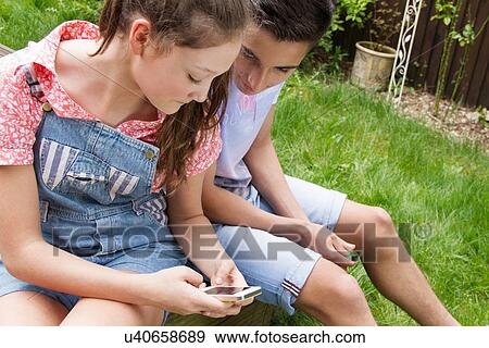 Stock Photo - Teenage couple looking at smartphone in garden. Fotosearch