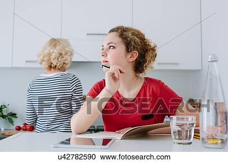 Stock Image - Teenage girl thinking about homework in kitchen. Fotosearch