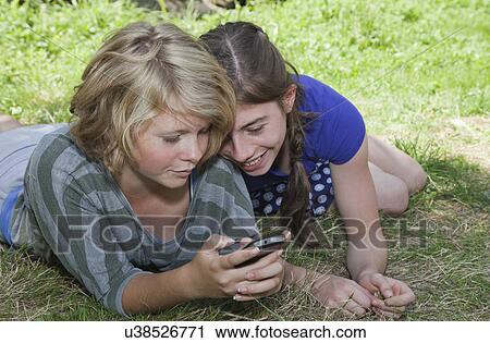 Teenage girls lying on grass, using smartphone View Large Photo Image Stock Image - Teenage girls lying on grass, using smartphone. Fotosearch
