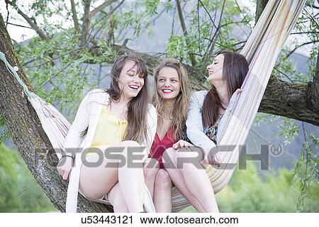 Stock Image - Three female friends sitting in a hammock, Piemonte, Italy. Fotosearch