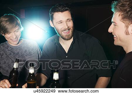 Stock Photo - Three male friends drinking bottled beer in nightclub. Fotosearch