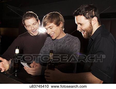 Three male friends looking at smartphone in nightclub View Large Photo Image Stock Image - Three male friends looking at smartphone in nightclub. Fotosearch
