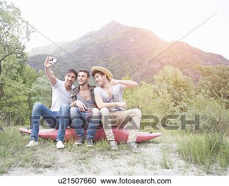 Three young men sitting on top of canoe, taking self portrait photograph View Large Photo Image Stock Image - Three young men sitting on top of canoe, taking self portrait photograph. Fotosearch