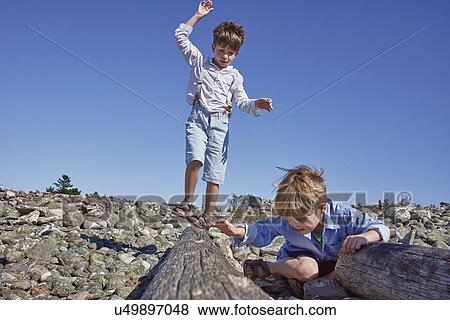 Stock Photo - Two boys playing on driftwood on beach. Fotosearch