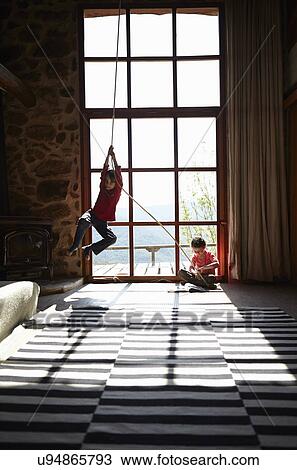 Two siblings in sitting room, brother on rope swing and sister reading View Large Photo Image Stock Image - Two siblings in sitting room, brother on rope swing and sister reading. Fotosearch