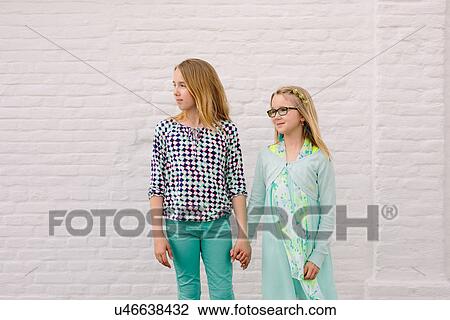Two sisters holding hands next to white wall View Large Photo Image Stock Image - Two sisters holding hands next to white wall. Fotosearch