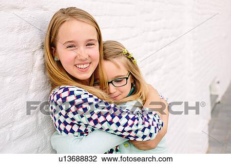 Two sisters holding hugging next to white wall View Large Photo Image Stock Image - Two sisters holding hugging next to white wall. Fotosearch