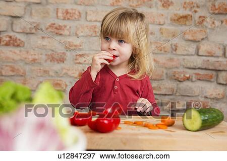 Two year old girl in kitchen eating raw vegetables View Large Photo Image Stock Photo - Two year old girl in kitchen eating raw vegetables. Fotosearch