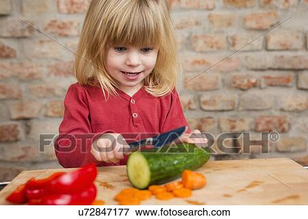 Two year old girl in kitchen learning to slice vegetables View Large Photo Image Stock Photo - Two year old girl in kitchen learning to slice vegetables. Fotosearch