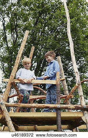 Stock Image - Two young brothers on top of tree house in forest. Fotosearch