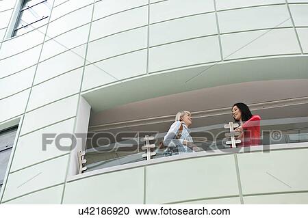 Two young women talking on balcony, low angle View Large Photo Image Stock Image - Two young women talking on balcony, low angle. Fotosearch
