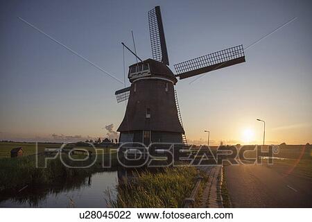 Stock Image - Windmill and waterway at sunset, Vollendam, Netherlands. Fotosearch