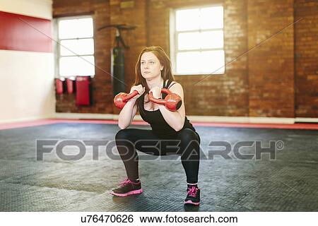 Stock Photograph - Woman squatting lifting kettlebells. Fotosearch
