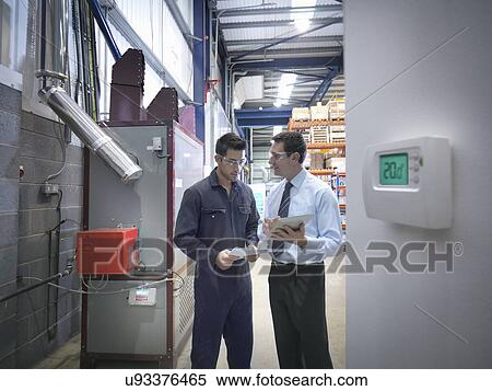 Stock Photography - Worker and office manager discuss energy use next to boiler in factory. Fotosearch