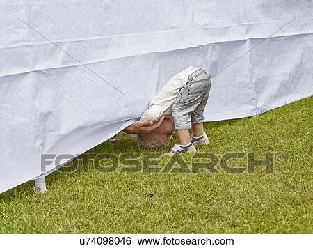 Stock Photograph - Young boy bending forward to reach fathers hand under tent. Fotosearch