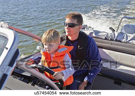 Young boy sitting on fathers lap steering motor boat View Large Photo Image Picture - Young boy sitting on fathers lap steering motor boat. Fotosearch