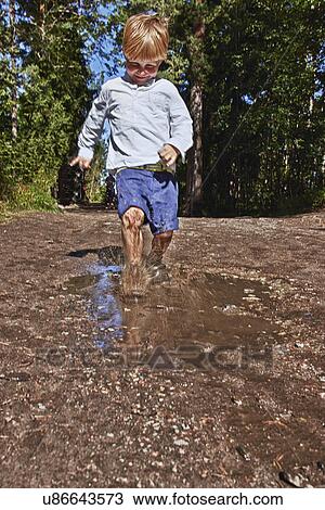 Stock Image - Young boy splashing in muddy puddle. Fotosearch