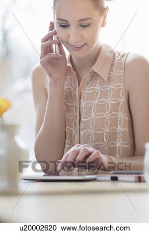 Stock Image - Young businesswoman in cafe chatting on smartphone and using digital tablet. Fotosearch