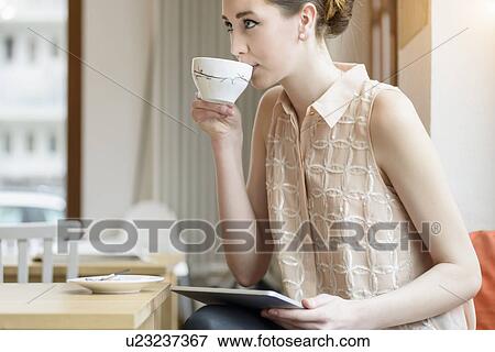 Young businesswoman in cafe drinking coffee and using digital tablet View Large Photo Image Stock Photo - Young businesswoman in cafe drinking coffee and using digital tablet. Fotosearch