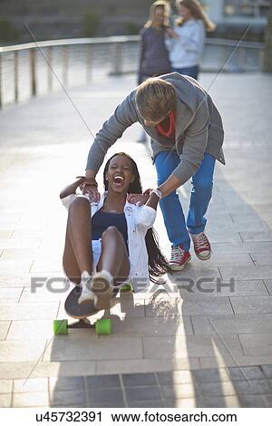 Young couple fooling around on skateboard at riverside View Large Photo Image Stock Image - Young couple fooling around on skateboard at riverside. Fotosearch