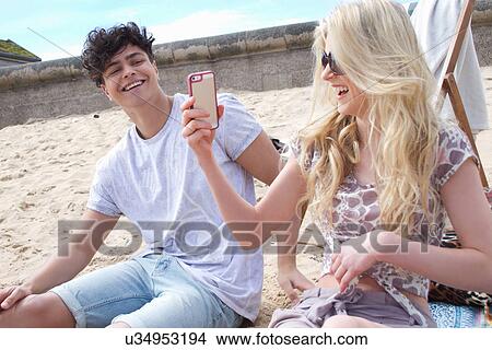 Picture -  Young couple looking at smartphone on beach. Fotosearch