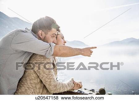 Stock Photo - Young couple looking at view of lake and mountains. Fotosearch