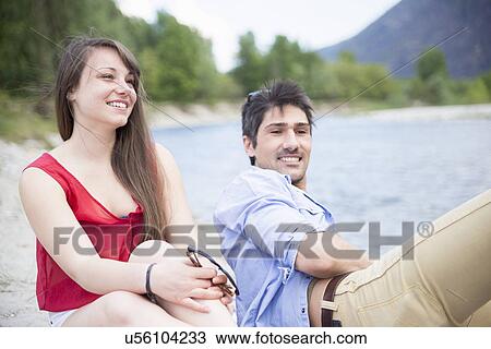 Young couple sitting by river View Large Photo Image Stock Image - Young couple sitting by river. Fotosearch