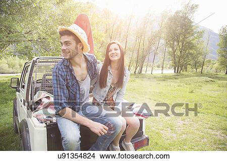 Picture - Young couple sitting on back of pick-up truck, Piemonte, Italy. Fotosearch