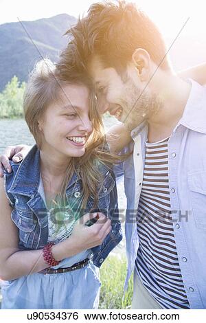 Young couple with arms around each other laughing View Large Photo Image Stock Photograph - Young couple with arms around each other laughing. Fotosearch